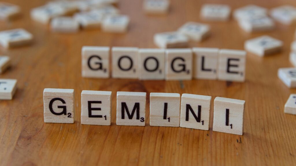 Scrabble tiles spelling out Google and Gemini on a wooden table, focusing on AI concepts.